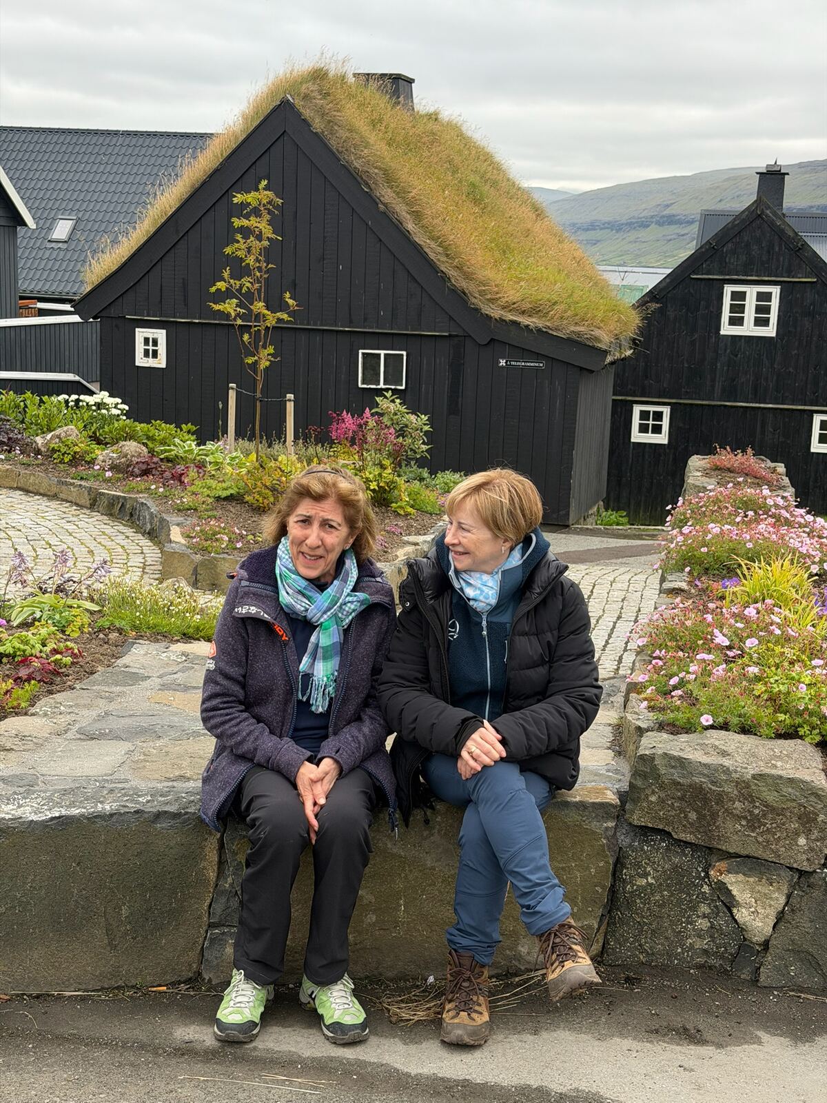 Dos personas sentadas en un muro en Eiði